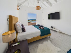 A modern bedroom with a bed, a TV, a bedside table, and a view of the outdoors.