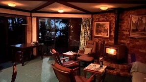 A cozy room with a fireplace, wooden furniture, and a large window. - Towering Gums (Lilli Pilli)