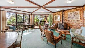 A spacious room with a large wooden table, multiple chairs, a fireplace, and a brick wall. - Towering Gums (Lilli Pilli)