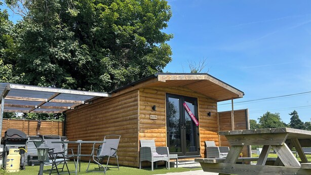 A wooden cabin with a glass door, outdoor seating, and a picnic table. -  Bambi's Hideaway (Castlewellan)