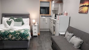 A compact bedroom with a bed, bedside table, and a small kitchenette in the background. -  Bambi's Hideaway (Castlewellan)
