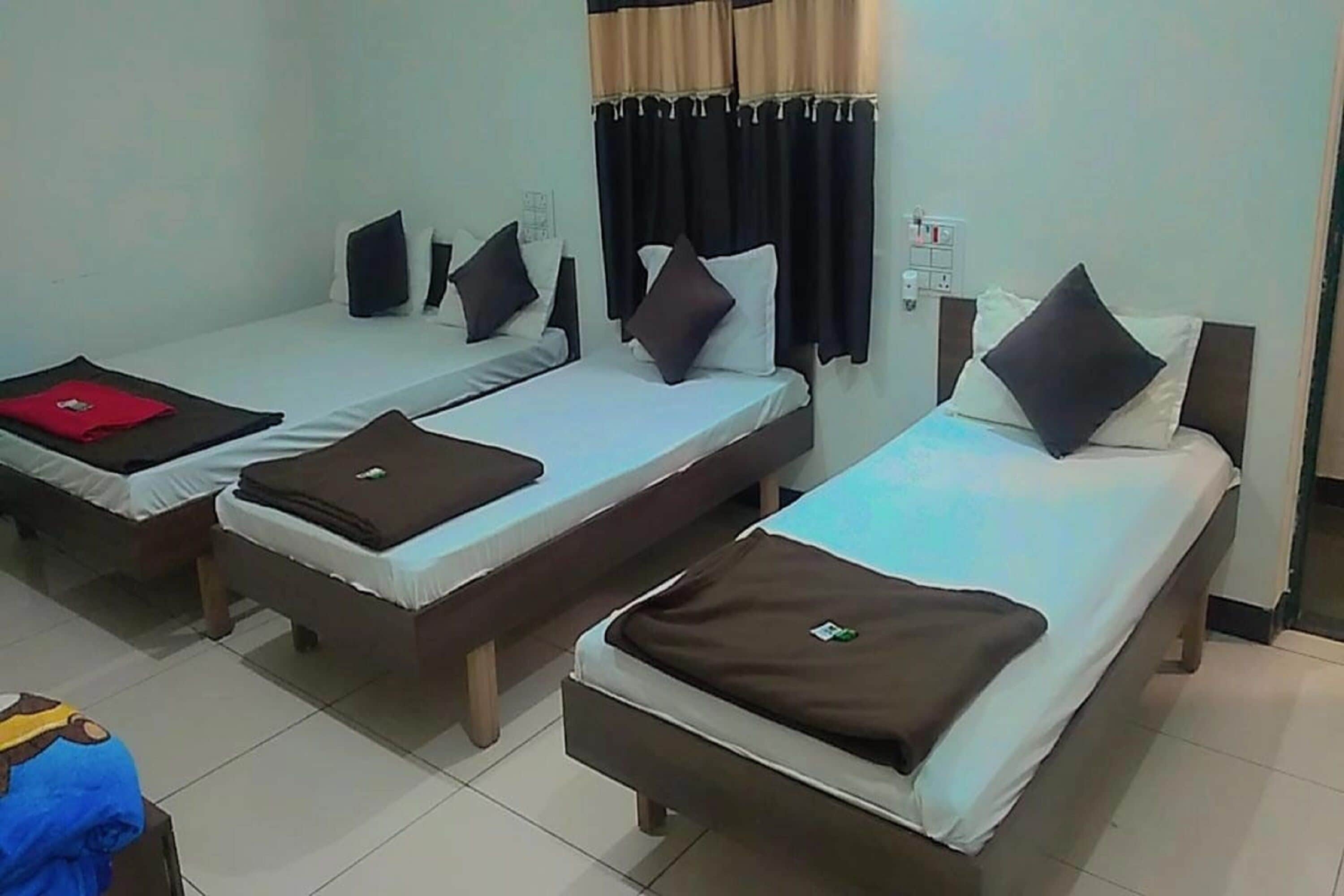 A hotel room with three single beds, each with a pillow and a blanket.