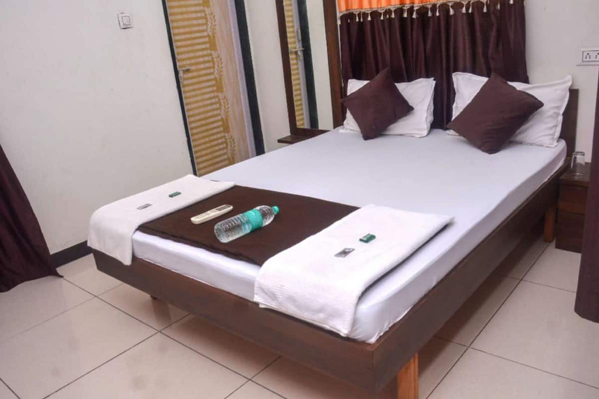 A neatly made bed with a white and brown color scheme, a bottle of water, and a remote control on the bed.