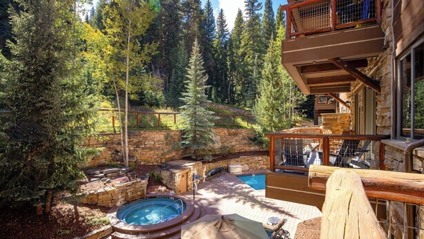 Ein Steinhaus mit Whirlpool, Pool und Sitzbereich im Freien, umgeben von Bäumen.