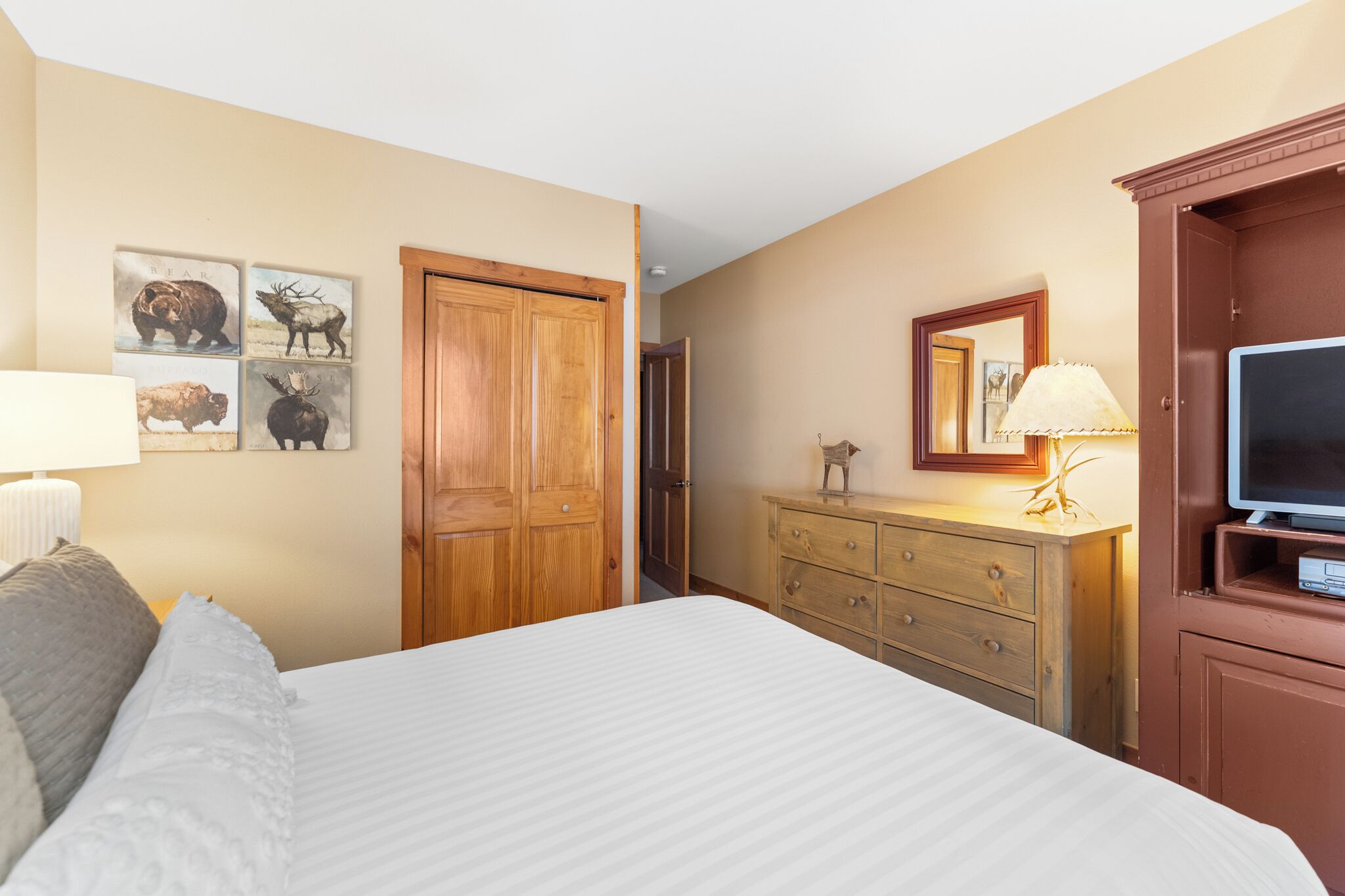 A hotel room with a large bed, wooden wardrobe, a television, and wall art depicting animals.