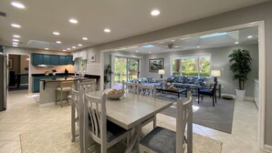 Amplia sala de estar con mesa y sillas de comedor, sofá y cocina con armarios color turquesa.