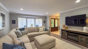 Una sala de estar con un sofá modular, un televisor de pantalla plana y una puerta que da a otra habitación.