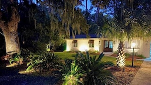 Una casa con un césped cuidado, un árbol grande y una palmera.