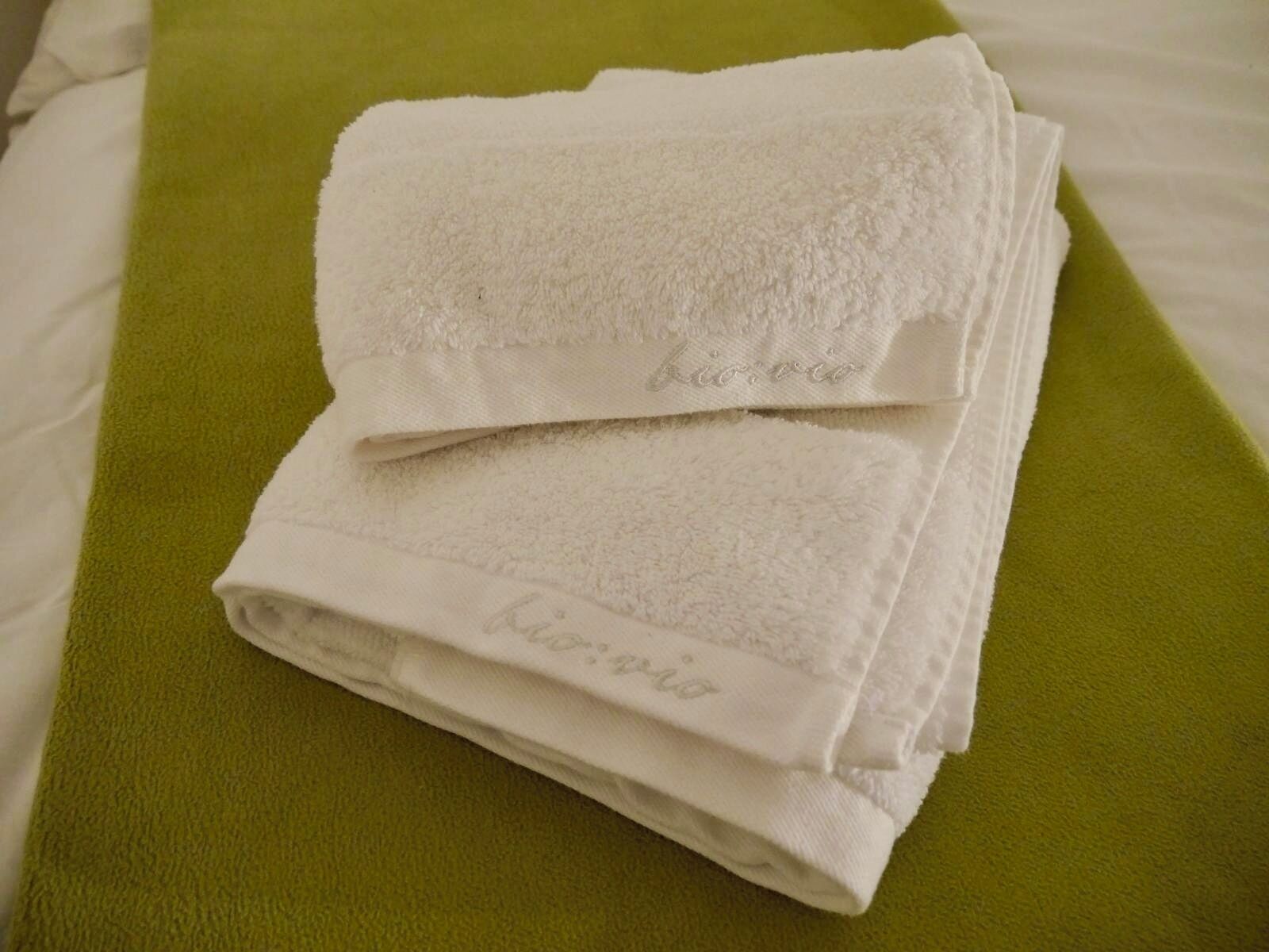 A stack of white towels with embroidered text on a green bedspread.