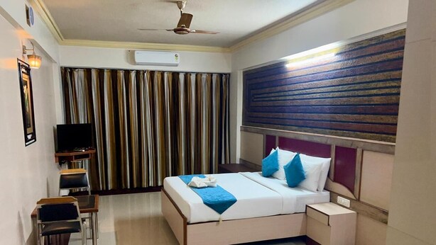 A hotel room with a bed, bedside table, chair, TV, and curtains. - The Grand Krishna Rooms (Bengaluru)