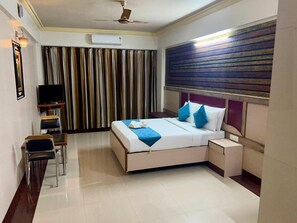 A hotel room with a bed, bedside table, chair, TV, and curtains. - The Grand Krishna Rooms (Bengaluru)