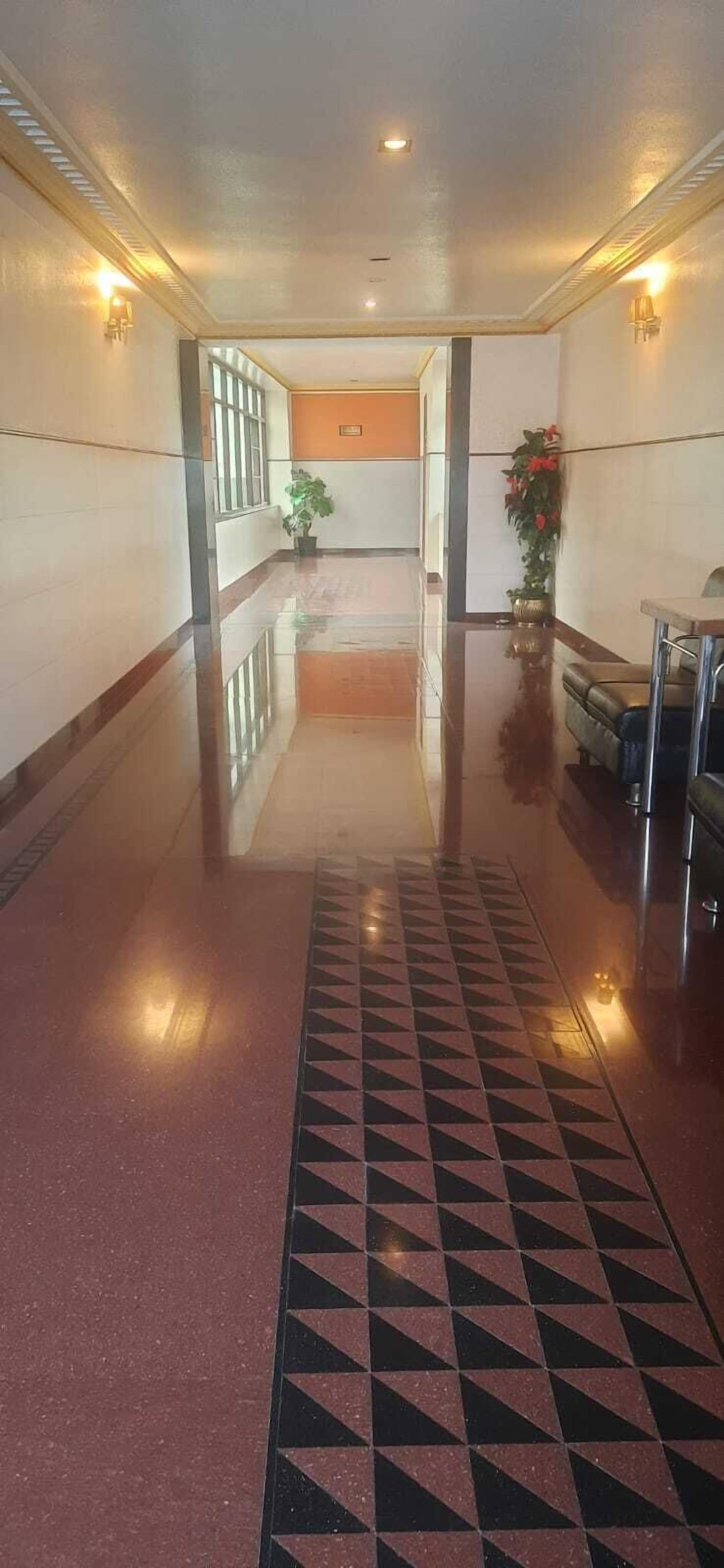 Un pasillo pulido con piso reflectante, un tapiz estampado y un mostrador de recepción con una planta.