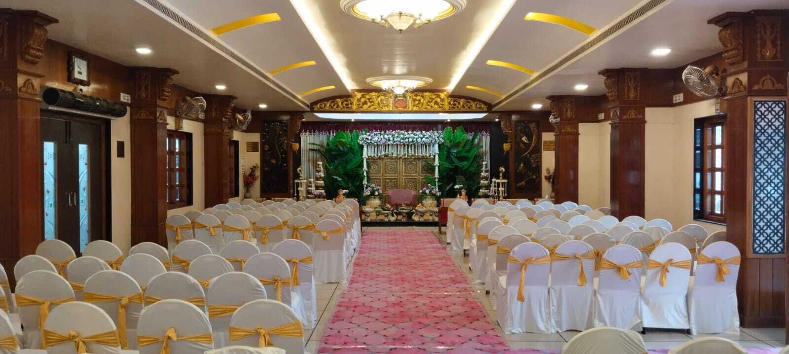 A formal event space with rows of white chairs with yellow sashes, a pink carpet, and ornate decorations.