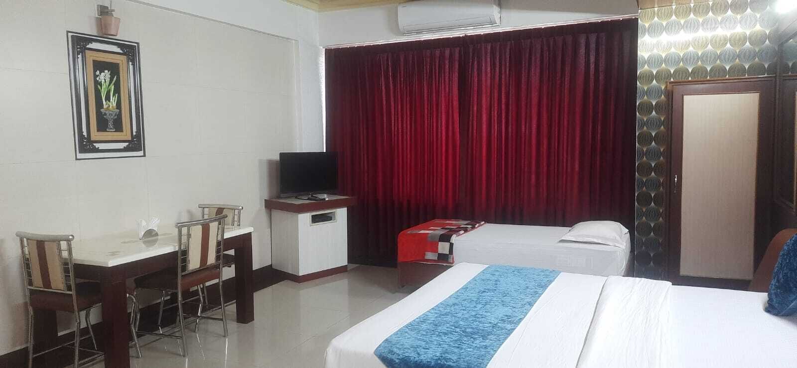 A hotel room with a bed, a desk with a chair, a television, and a red curtain.