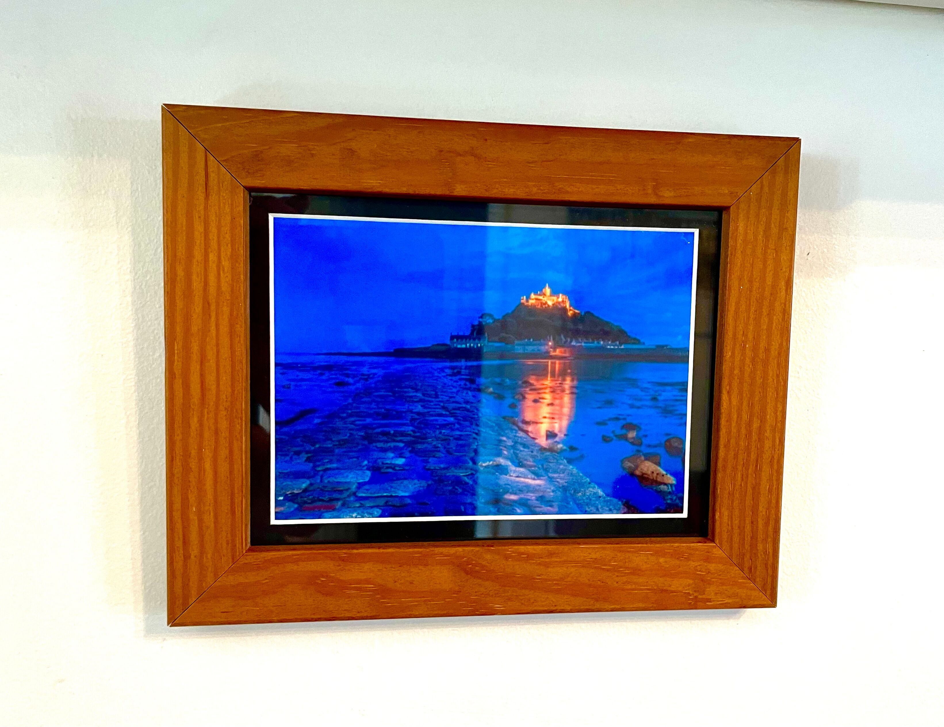 A framed photograph of a castle on a hill with a body of water in front, reflecting the castle.