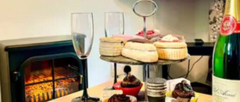 Ein Esstisch mit verschiedenen Desserts, einer Champagnerflasche und einem Kamin im Hintergrund.