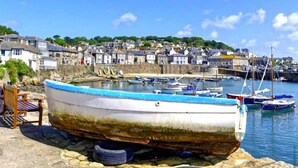 A coastal town with a row of houses, a harbor with boats, and a small boat on land. - 2 Bedrooms Cornish Holidays For Penzance & St Ives (Penzance)