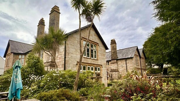A stone building with multiple chimneys, a garden with various plants, and a wooden bench. - 2 Bedrooms Cornish Holidays For Penzance & St Ives (Penzance)