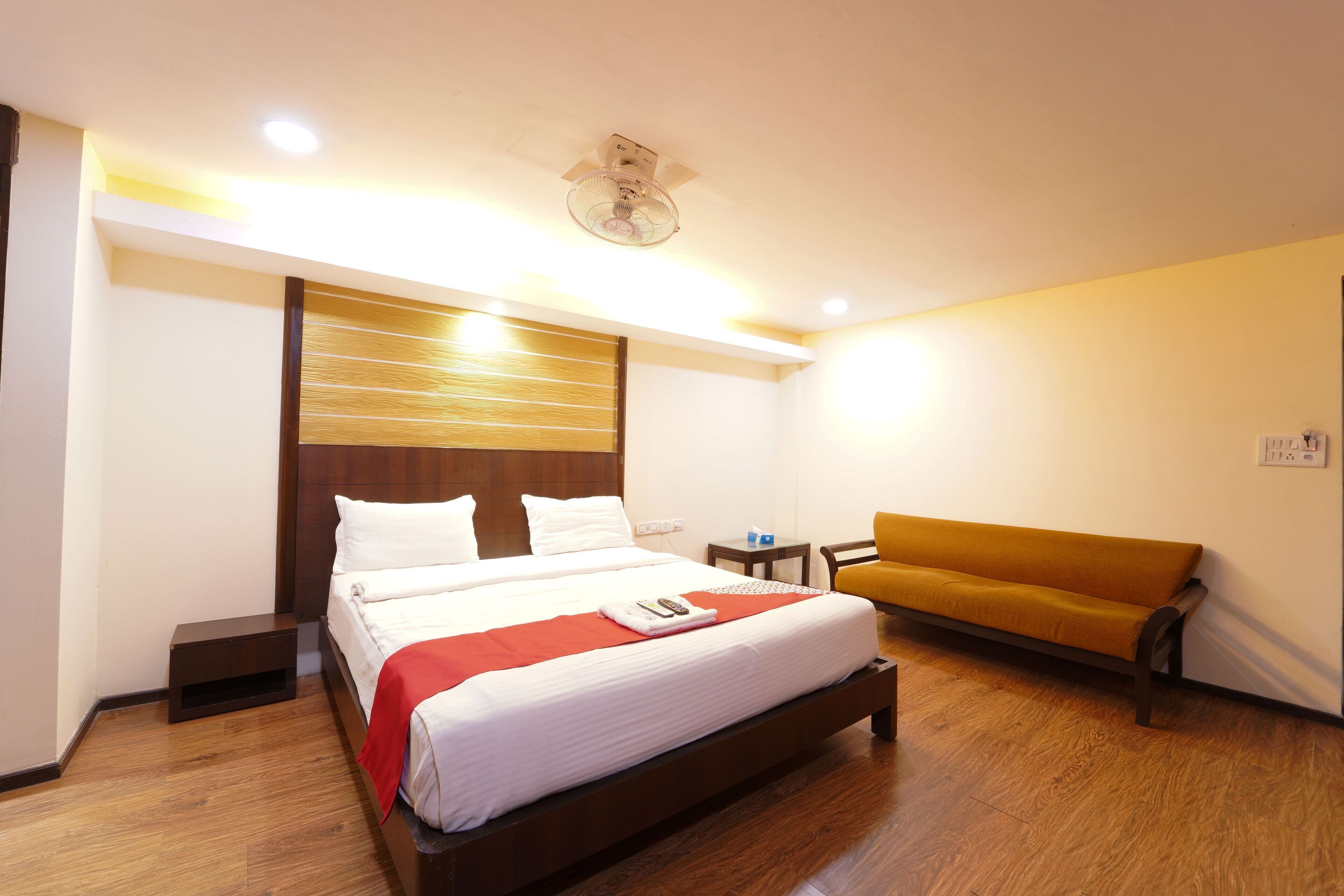 A hotel room with a large bed, a small table, a bench, and a ceiling fan.