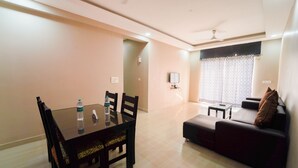 A dining area with a table and chairs, a sofa, and a TV on the wall. - Ocean View The Apartment Hotel (Consua)