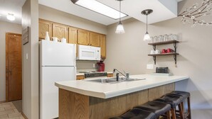Une cuisine avec des meubles en bois, un réfrigérateur blanc, un four à micro-ondes, une cuisinière, un évier et un coin bar avec des tabourets.
