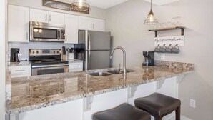 A modern kitchen with white cabinets, stainless steel appliances, granite countertops, and bar stools. - Troon Golf View | Golf Course View | On-site Amenities (Branson)