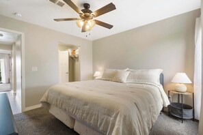 A bedroom with a bed, ceiling fan, bedside lamps, and a door leading to another room. - Troon Golf View | Golf Course View | On-site Amenities (Branson)