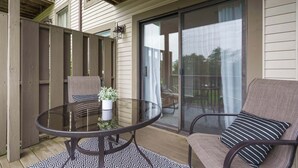 A patio with a glass table and chairs, a potted plant, and a sliding glass door leading to a deck. - Troon Golf View | Golf Course View | On-site Amenities (Branson)