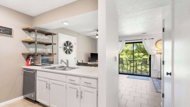 A modern kitchen with white cabinets, a dishwasher, a built-in oven, and a window overlooking a balcony.