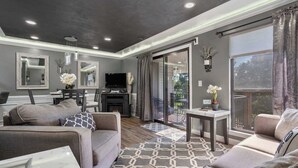 Una sala de estar moderna con chimenea, sofás, televisor y un balcón con cortinas.