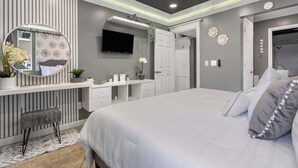 Un dormitorio moderno con una cama grande, un tocador con espejo y un televisor sobre el aparador.