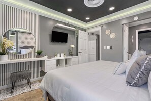A bedroom with a bed, a vanity with a mirror, a television, and a door leading to a bathroom.