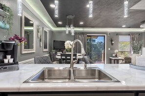 A modern kitchen with a large sink, pendant lights, and a dining area with a round table and chairs.