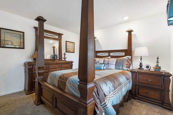 A four-poster bed with a headboard, a nightstand with a lamp, and a dresser with drawers.