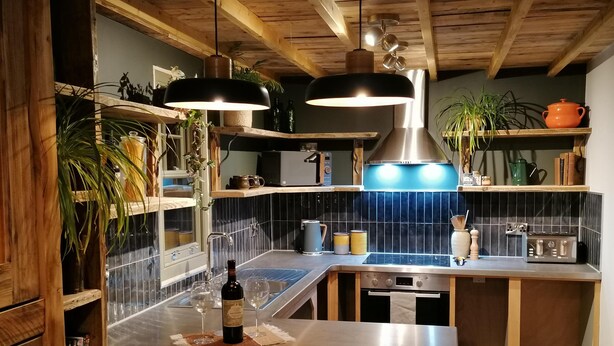 Une cuisine moderne avec des poutres en bois, un dosseret de carreaux noirs, des appareils en acier inoxydable et des étagères en bois.