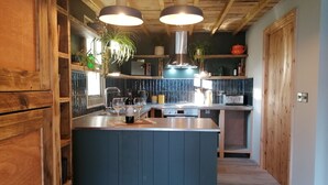 Une cuisine moderne avec des poutres en bois, un îlot central, des luminaires suspendus et une vue sur la salle à manger.