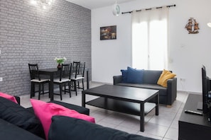 A living room with a dining area, a gray sofa, a gray couch, a coffee table, and a TV stand.