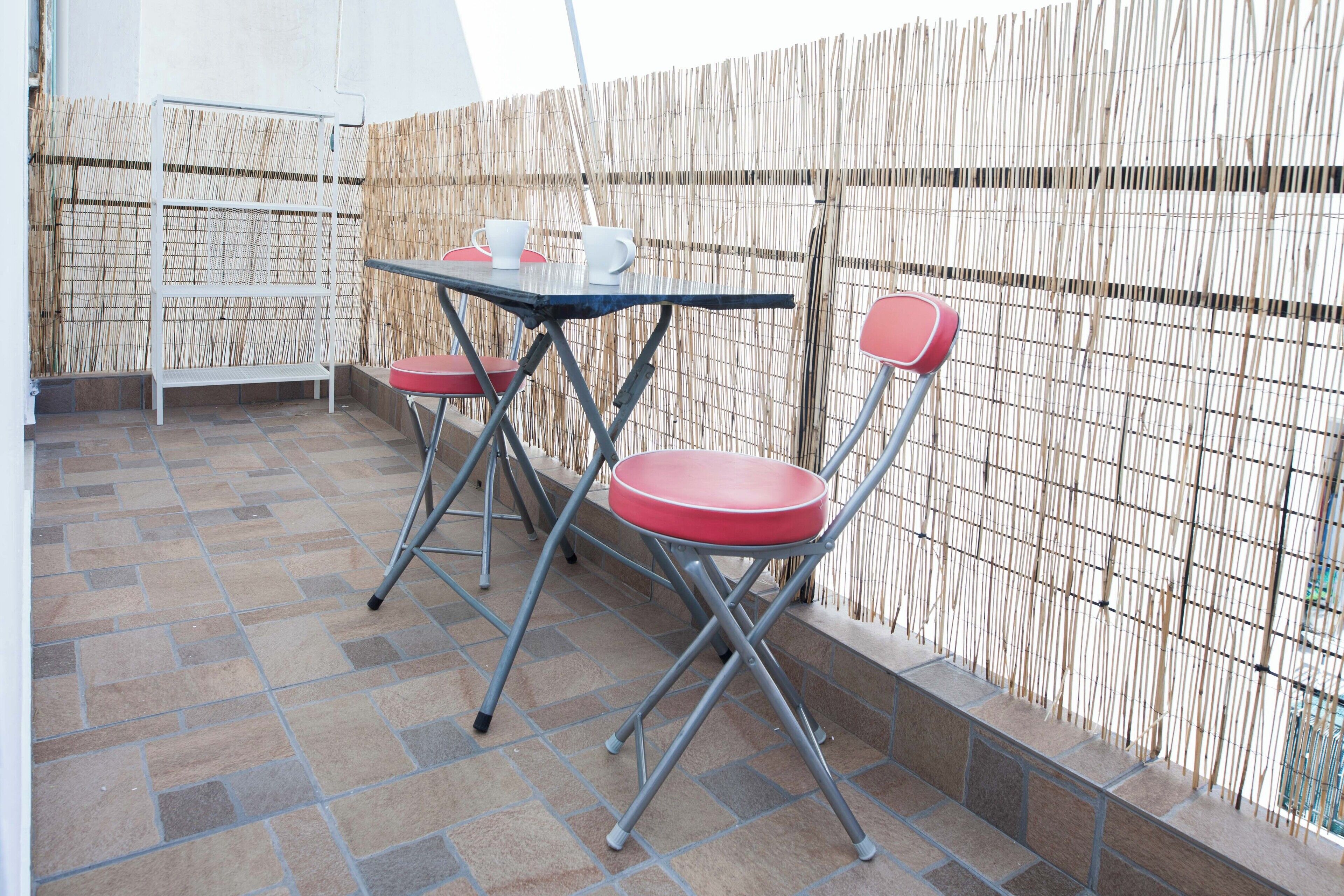 An outdoor patio with a table and two chairs, a bamboo fence, and a tiled floor.