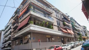 Un edificio residencial de varios pisos con balcones, equipos de aire acondicionado y un estacionamiento con automóviles.