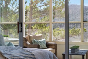 Relax in a serene room with a forest view, featuring a comfortable sofa, a small side table, and a neatly made bed.