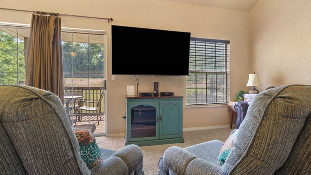 Een woonkamer met twee grijze fauteuils, een blauwgroene kast met een flatscreen-televisie, en een raam met zonwering.