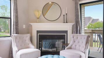 A living room with a fireplace, two armchairs, a round mirror, and a view of the outside.