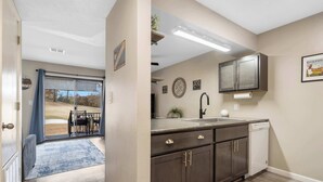 A kitchen with dark cabinets, a sink, and a dishwasher. There is a window with a view of a golf course. - Greenside Retreat: Pointe Royale (Branson)
