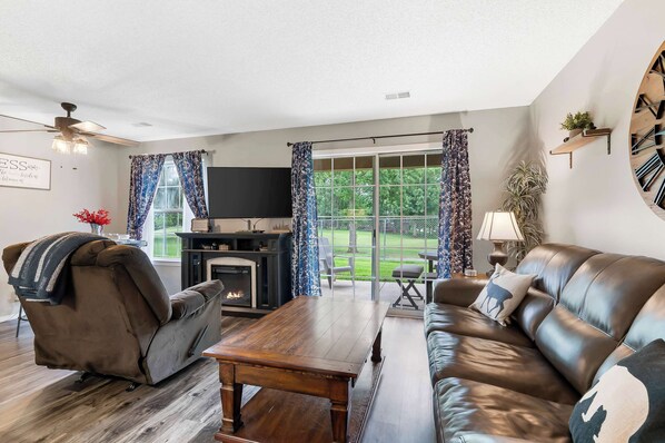 A modern living room with a fireplace, leather sofa, and a large window with curtains.