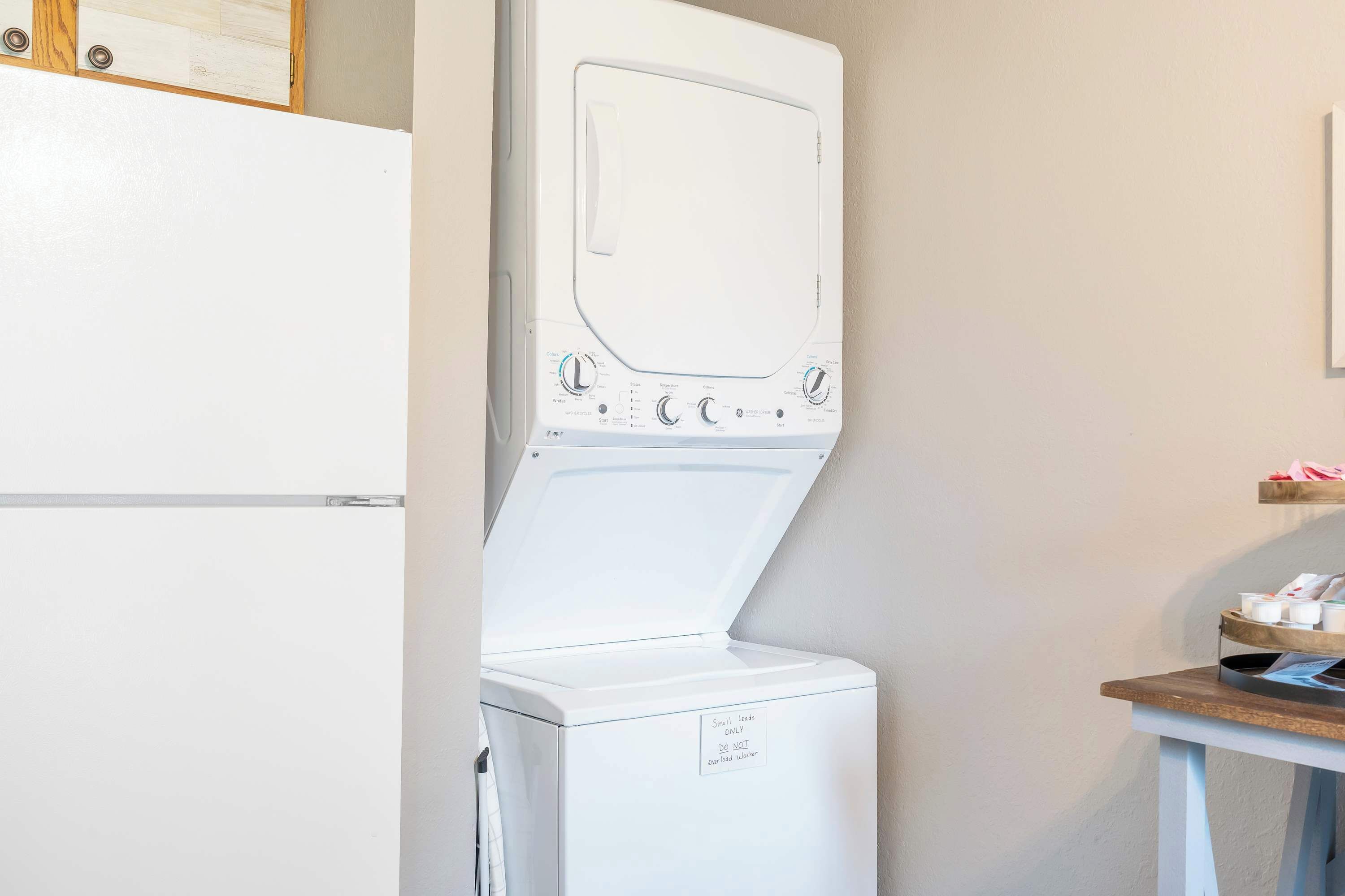 Una lavadora blanca con un panel de control, una mesita con artículos de aseo, y un mueble de madera encima.