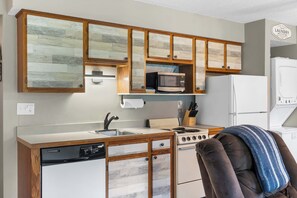 A compact kitchen with wooden cabinets, a microwave, a stove, and a dishwasher.