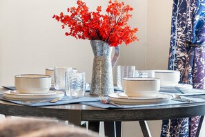 A dining table set with white plates, bowls, and clear glassware, accompanied by a vase of red flowers.