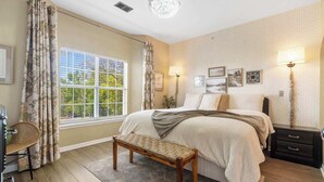 A bedroom with a large bed, two bedside tables with lamps, a bench, a window with curtains, and wall art. - Fairview Escape | Holiday Hills Branson | Golf | Outdoor Pools (Branson)