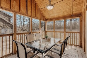 A sunroom with a glass table and chairs, wooden walls, and large windows. - Cozy Pines Cabin | Gated Community | Pool + Golf Course | Near SDC (Branson West)