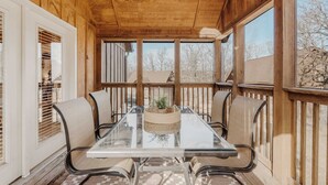 A wooden deck with a glass table and chairs, a ceiling fan, and a view of the outside.